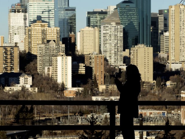 A pedestrian stops to take photos of the Edmonton skyline, Dec. 24, 2023. 