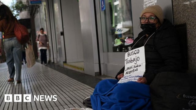 Unemployed Viviana Quevedo, 57, sits on a street holding a sign that reads "I am looking for a job in order to be able to rent" in Buenos Aires, 25 September 2024