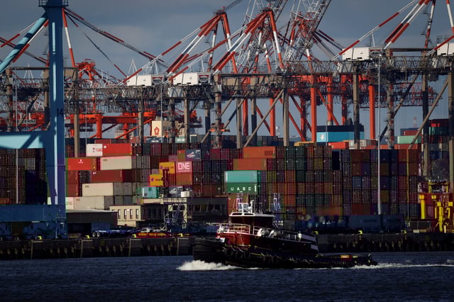 A tugboat passes shipping containers being unloaded and stacked on a pier at Port Newark, New Jersey, U.S., November 19, 2021. REUTERS/Mike Segar/File Photo