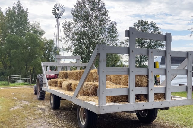 A tractor pulling a wooden cart filled with dried hay bales for fall harvest hayrides. 