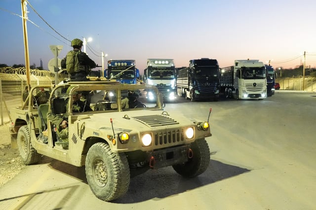 Israeli soldiers sit in a military vehicle near trucks carrying humanitarian aid that wait before making their way to the Gaza Strip, amid the ongoing conflict in Gaza between Israel and Hamas, at Erez Crossing in southern Israel, October 21, 2024. REUTERS/Janis Laizans
