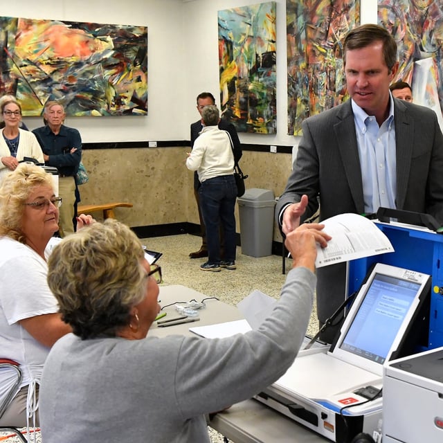 Kentucky Governor Andy Beshear, center, receives is ballot from a poll worker as his wife First Lady Britainy Beshear looks on during early voting at Yes Arts in Louisville, Ky., Thursday, Oct. 31, 2024. (AP Photo/Timothy D. Easley)