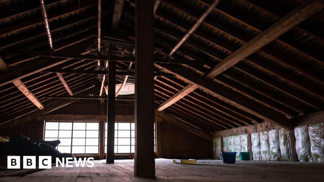 A dark attic with wood wooden beams, lit only by a small window