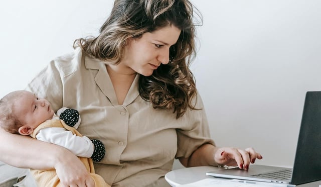 woman working on laptop while holding a baby