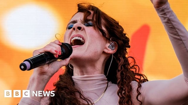 Kate Nash singing on stage against an orange backdrop