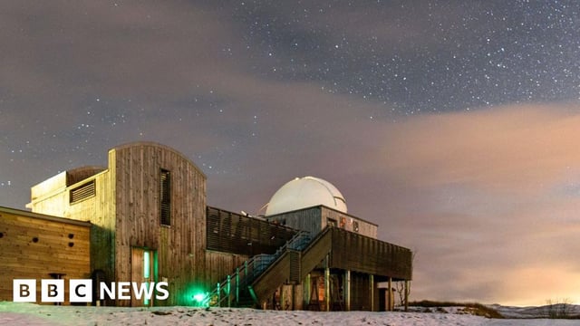 A wooden-fronted observatory building on snowy ground underneath a very starry sky