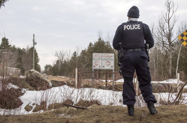 A police officer looks into the United States as she stands on the Canadian side of the border near Hemmingford, Que., Feb. 23, 2017. THE CANADIAN PRESS/Paul Chiasson