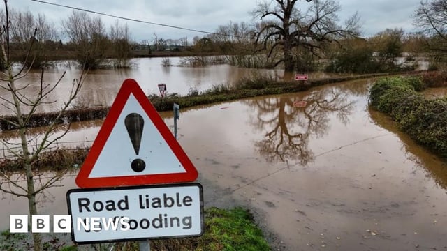 Widespread flooding near Upton-on-Severn, after Storm Bert. In the foreground, a warning sign advises that the road is liable to flooding and indeed, both the road and all surrounding fields are submerged under brown, muddy water.