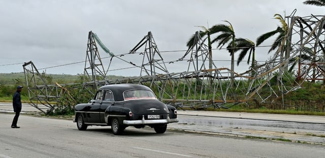Une voiture passe devant un pylône électrique abattu lors du passage de l’ouragan Rafael sur la route reliant Artemisa à La Havane, le 7 novembre 2024 à Cuba