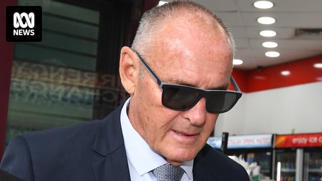 A man wearing dark glasses walking outdoors with his head bowed.