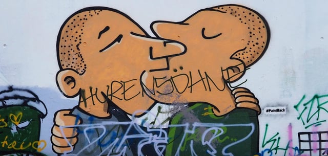 Beschmiertes Graffito von zwei sich küssenden Männern in Berlin-Kreuzberg