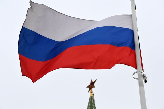 A Russian flag flies in front of a ruby star atop one of the Kremlin's towers in downtown Moscow.