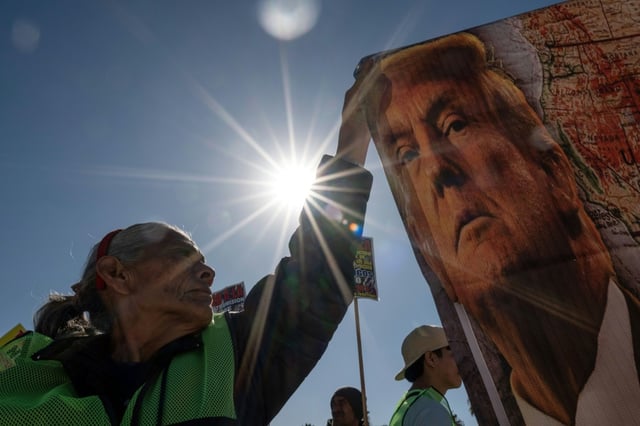 A demonstrator at a Mexico-US border crossing in Tijuana holds a banner with the image of US President-elect Donald Trump, who has vowed a mass deportation of undocumented immigrants