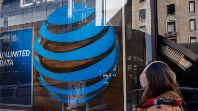 A pedestrian walks past a large AT&T logo on the glass exterior of an AT&T store.