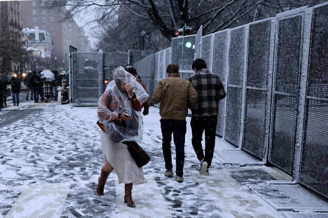 A woman steels herself against a blast of winter weather as she walks along security fencing outside the White House the day before President-elect Donald Trump's inauguration on Jan. 19, 2025.