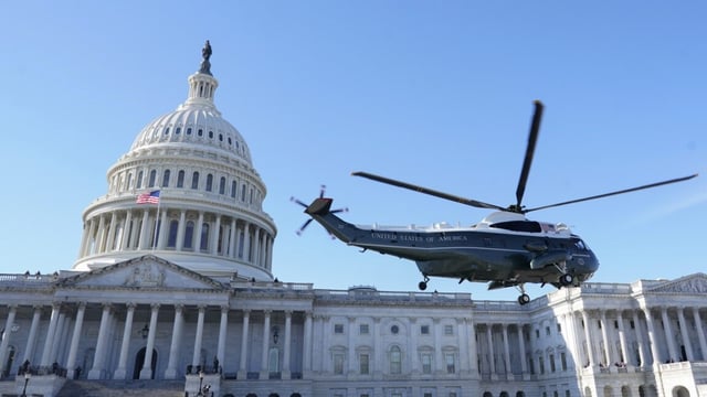 A helicopter with the words "United States of America" and a US flag lifts off in front of the US Capitol building