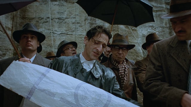 Adrien Brody holding a large blueprint in A24's The Brutalist