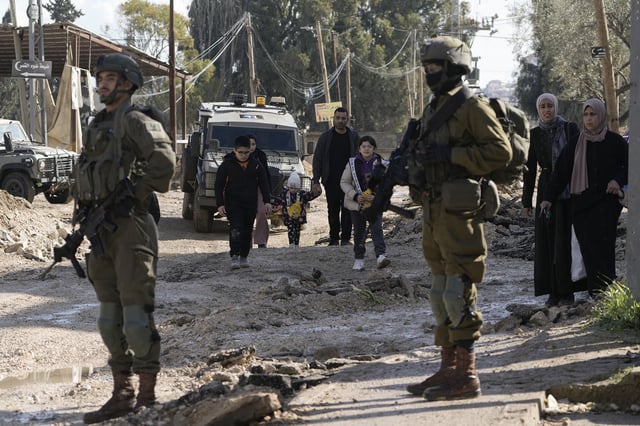 Israeli soldiers stand guard as Palestinians displaced by an Israeli military operation evacuate from the Jenin refugee camp in the West Bank on Thursday.