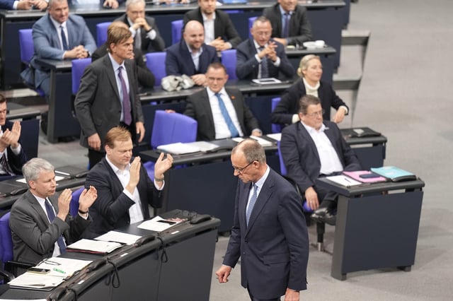 Friedrich Merz läuft im Bundestag an der AfD-Fraktion vorbei, die nach der Bekanntgabe der Ergebnisse der Abstimmung für eine Verschärfung der Migrationspolitik jubelt und klatscht