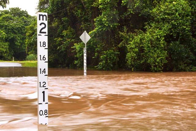 A stock image of a flooded road in Queensland, Australia, with depth indicators in the water.