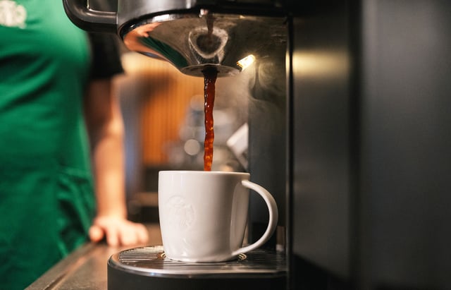 A Starbucks barista fills up a cup of coffee in a ceramic mug.