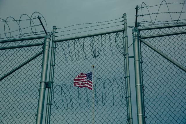 GUANTANAMO BAY, CUBA - JUNE 27: An American flag flies behind barbed wire fencing at the Office of Military Commissions building on June 27, 2023 at Guantanamo Bay, Cuba.