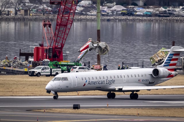 A crane offloads a piece of wreckage from a salvage vessel onto a flatbed truck, near the wreckage site in the Potomac River of a mid-air collision between an American Airlines jet and a Black Hawk helicopter, at Ronald Reagan Washington National Airport, Wednesday, Feb. 5, 2025, in Arlington, Va. (AP Photo/Ben Curtis)