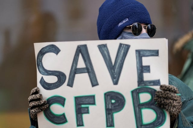 A demonstrator holds a sign, during a protest, the day after members of Elon Musk's Department of Government Efficiency (DOGE) moved into the Consumer Financial Protection Bureau (CFPB), in Washington, U.S. February 8, 2025. REUTERS/Nathan Howard/File Photo