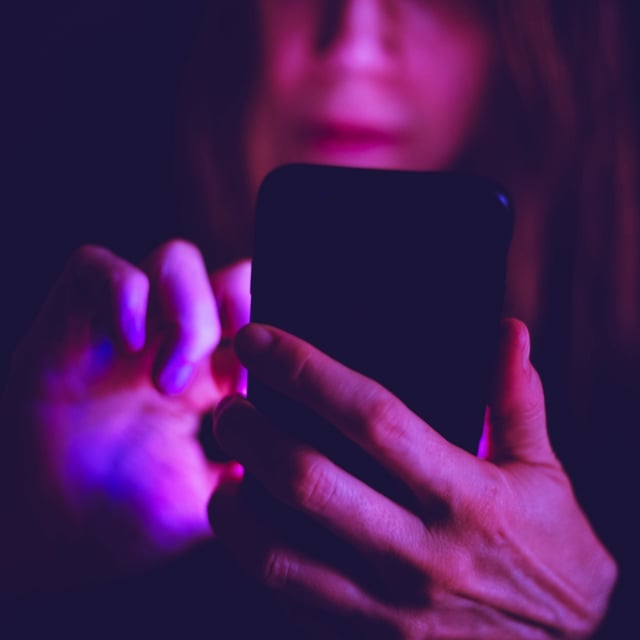 A woman using smartphone at night under colorful LED lights