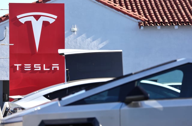 The Tesla logo is displayed at a Tesla dealership near a parked Cybertruck (BOTTOM) on January 2, 2025 in Alhambra, California.