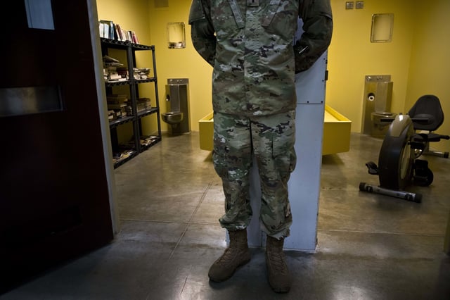 FILE - In this photo reviewed by U.S. military officials, a U.S. soldier stands between two cells, one used as a library and the other a gym, inside the Camp VI detention facility at the Guantanamo Bay U.S. naval base in Cuba, June 6, 2018. (AP Photo/Ramon Espinosa, File)