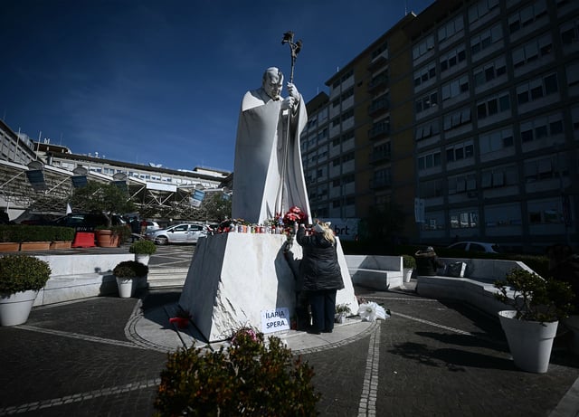A woman leaves a rosary at the feet of a statue of late Pope John Paul II, on Friday, outside Agostino Gemelli Polyclinic in Rome, Italy. Pope Francis spent his seventh day there, being treated for pneumonia.