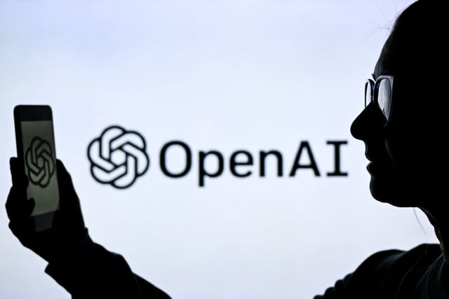 A woman holds a cell phone in front of a computer screen displaying the Open AI logo, on Feb. 10, in Edmonton, Canada.