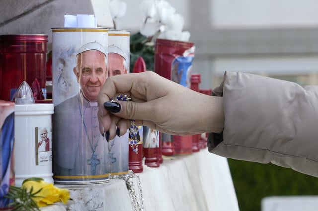 A woman lays a rosary near candles adorned with pictures of Pope Francis outside the Agostino Gemelli Polyclinic where Pope Francis is battling pneumonia, in Rome, Saturday, Feb. 22, 2025, (AP Photo/Gregorio Borgia)