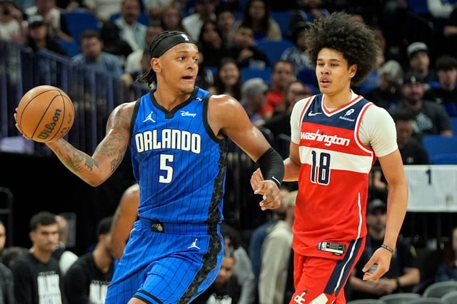 Orlando Magic forward Paolo Banchero (5) passes the ball around Washington Wizards forward Kyshawn George (18) during the first half of an NBA basketball game, Sunday, Feb. 23, 2025, in Orlando, Fla. (AP Photo/John Raoux)