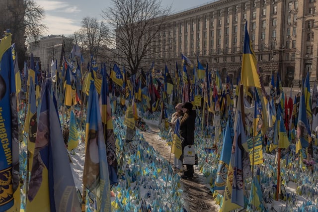 Visitors stand next to a makeshift memorial paying tribute to Ukrainian and foreign fighters at Independence Square in Kyiv ahead of the third anniversary of Russia's invasion of Ukraine.