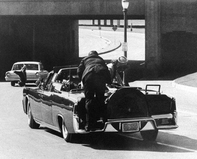 Secret Service Agent Clint Hill rides on the back of the presidential limousine after President John F. Kennedy was fatally shot in Dallas, Texas, on November 22, 1963. First lady Jacqueline Kennedy leans over the president.