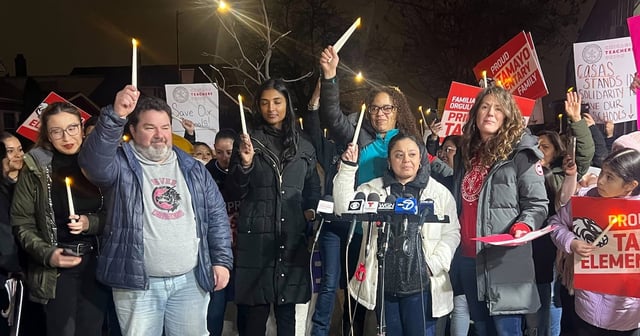 A group of people stand outside at night holding candles during a vigil.