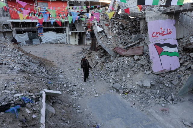 A Palestinian walks past graffiti and the rubble of buildings, ahead of the holy fasting month of Ramadan, amid a ceasefire between Israel and Hamas, in Khan Younis, in the southern Gaza Strip, February 27, 2025. REUTERS/Ramadan Abed/File Photo