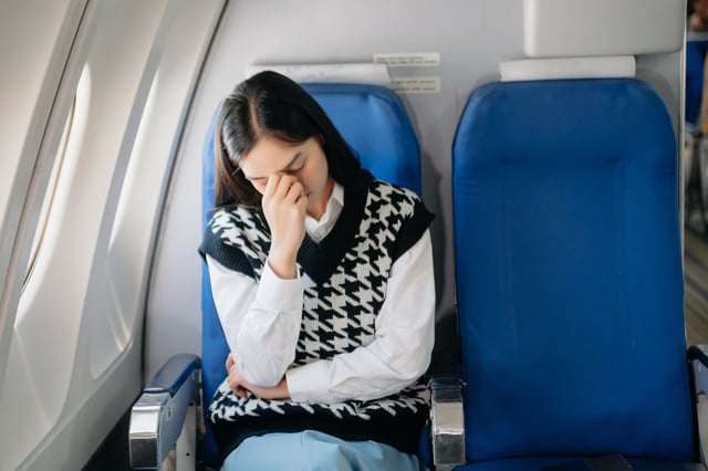 A woman on a plane puts her head in her hands.