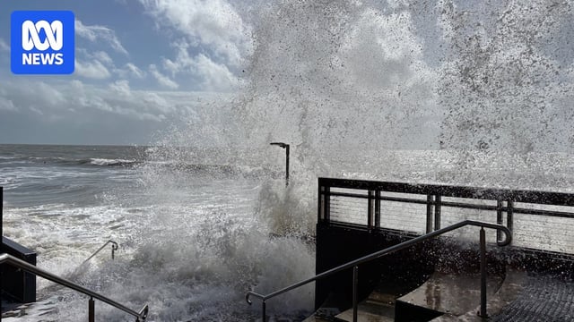 A wave crashes over a beach walkway.
