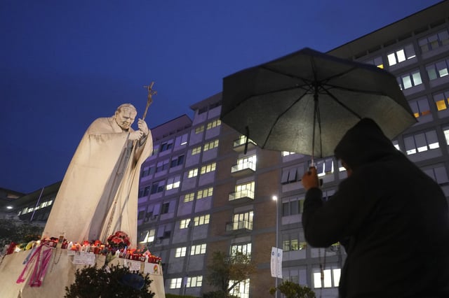A man shelters from the rain as he prays for Pope Francis in front of the Agostino Gemelli Polyclinic, where the Pontiff has been hospitalized since Feb.14, in Rome, Saturday, March 1, 2025. (AP Photo/Kirsty Wigglesworth)