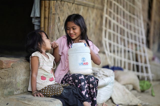 A Rohingya girl feeds a child from a jar with the USAID logo on it, at a refugee camp in Cox's Bazar, Bangladesh, February 11, 2025. REUTERS/Ro Yassin Abdumonab/File Photo