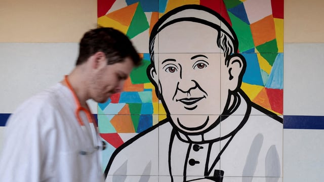 A man walks near a painting depicting Pope Francis at the Gemelli Hospital, where he is admitted for treatment, in Rome, Italy, March 3, 2025.