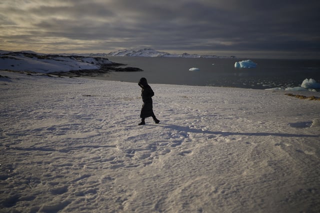 A woman walks along the shore of a beach while pieces of ice float in the sea of Nuuk, Greenland, Friday, Feb. 14, 2025. (AP Photo/Emilio Morenatti)