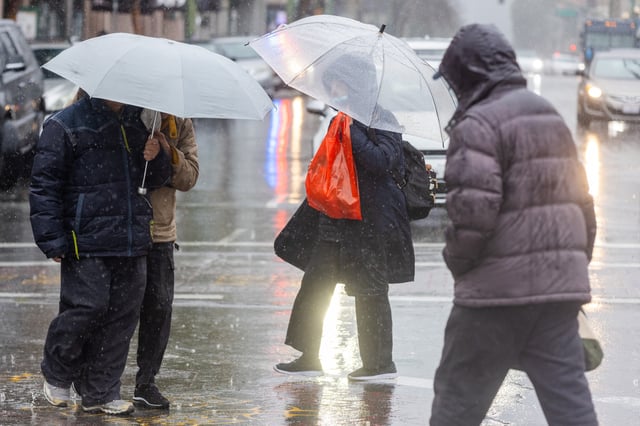 Pedestrians use an umbrella to shield themselves from the rain while crossing the street in Chinatown during a heavy downpour in Oakland, Calif., on Feb. 13, 2025.