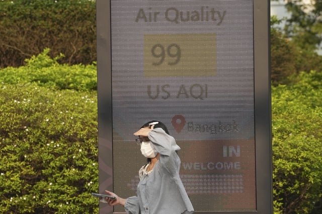FILE - A pedestrian wears a face mask in front of a sign displaying an Air Quality Index in Bangkok, Thailand, Feb. 6, 2025. (AP Photo/Sakchai Lalit, File)