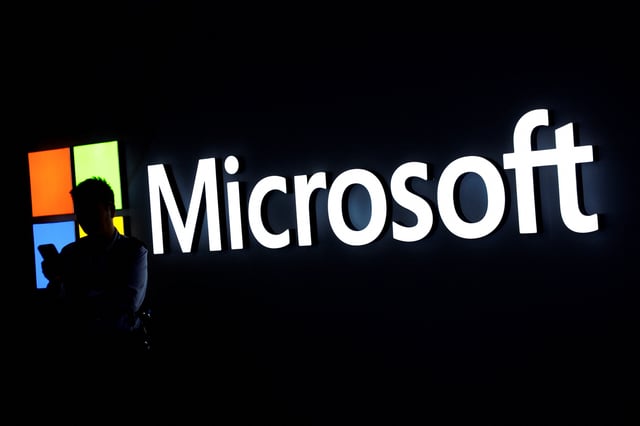 A man looks at his phone in front of the Microsoft logo during the 2025 Mobile World Congress (MWC) in Barcelona, Spain, March 3, 2025. REUTERS/Albert Gea/File Photo