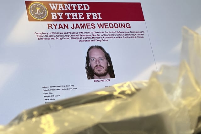 FILE - An image of former Canadian Olympic snowboarder Ryan Wedding, who is a fugitive and been charged with allegedly running and participating in a transnational drug trafficking operation, is displayed on a video monitor along with bricks of cocaine, foreground, during a news conference at the FBI offices in Los Angeles, Oct. 17, 2024. (AP Photo/Damian Dovarganes, File)