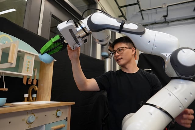 Graduate student Felix Yanwei Wang nudges a robotic arm that is manipulating a bowl in a toy kitchen set up in the group’s lab. Using the framework Wang and his collaborators developed, slightly nudging a robot is one way to correct its behavior.